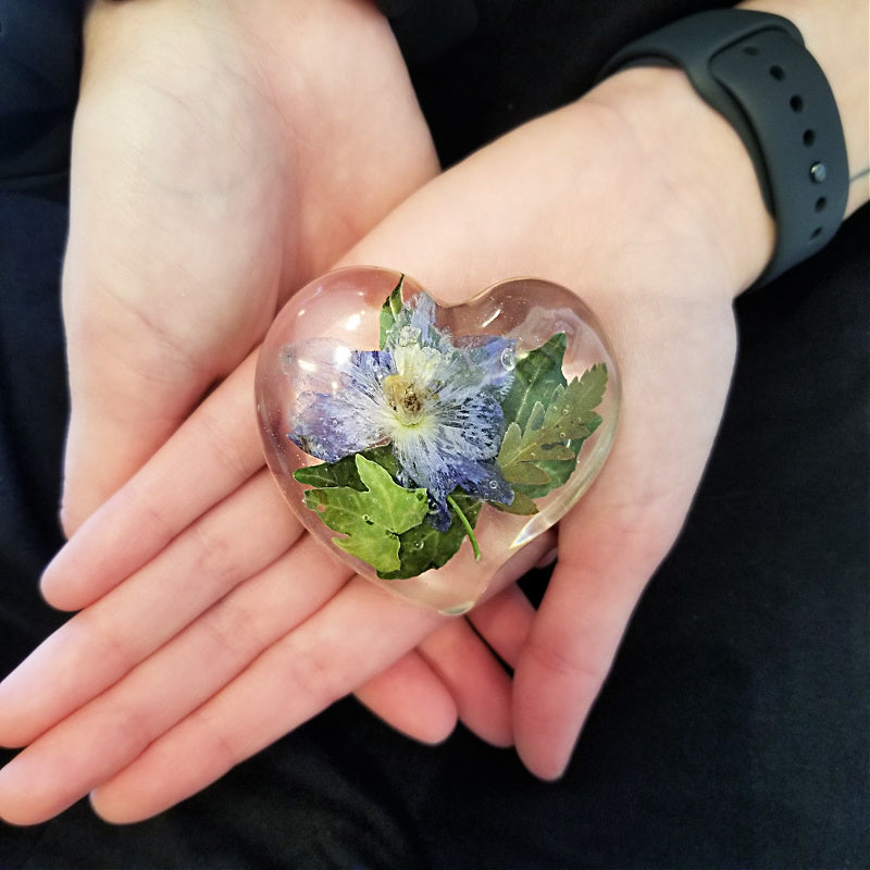 Model gently holding a medium resin heart filled with preserved flowers.