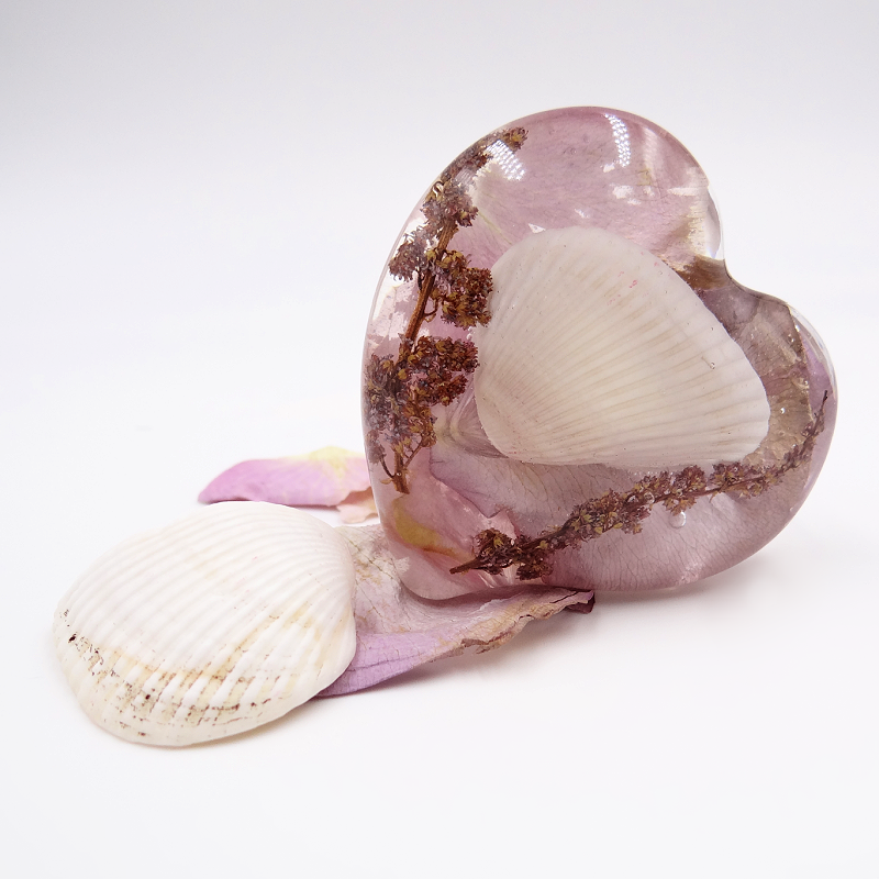 Preserved pink flowers and seashells encased in a resin heart keepsake.