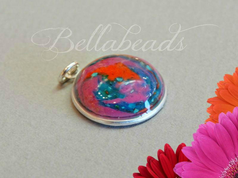 Sterling silver round pendant with a read, pink, and blue clay swirled with ashes.