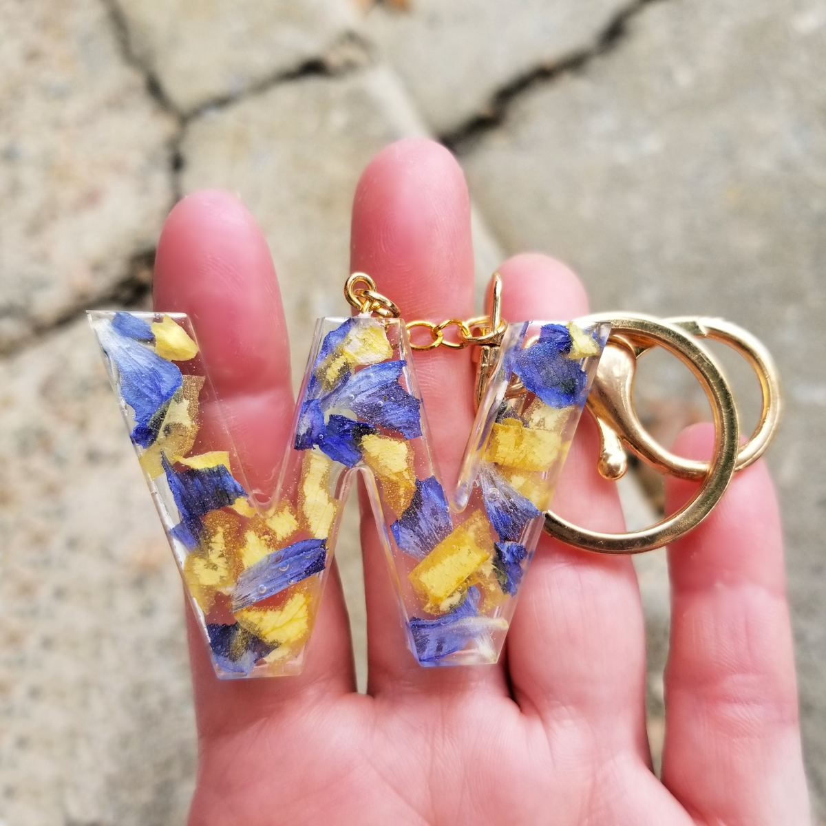 Model holding resin letter W keychain with preserved yellow and blue flowers, showing size reference