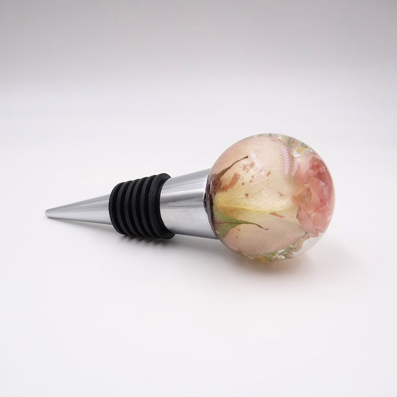 Resin wine stopper featuring a preserved miniature pink rose, a delicate floral keepsake for weddings or memorials.