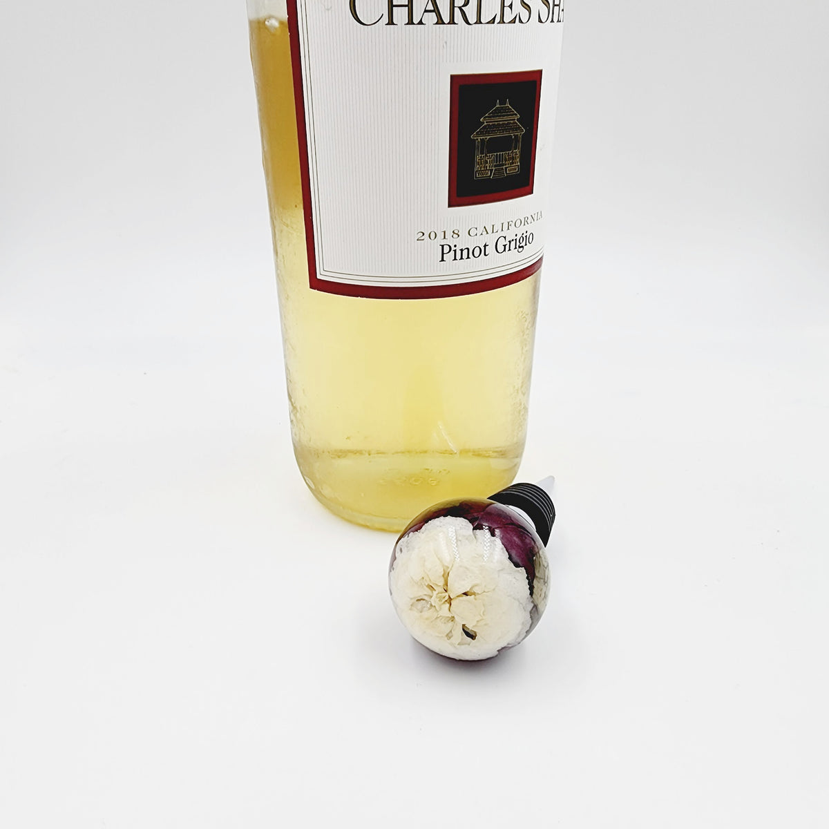 Floral resin wine stopper made with preserved white flowers, displayed with a wine bottle as a functional and elegant keepsake for weddings or memorials.